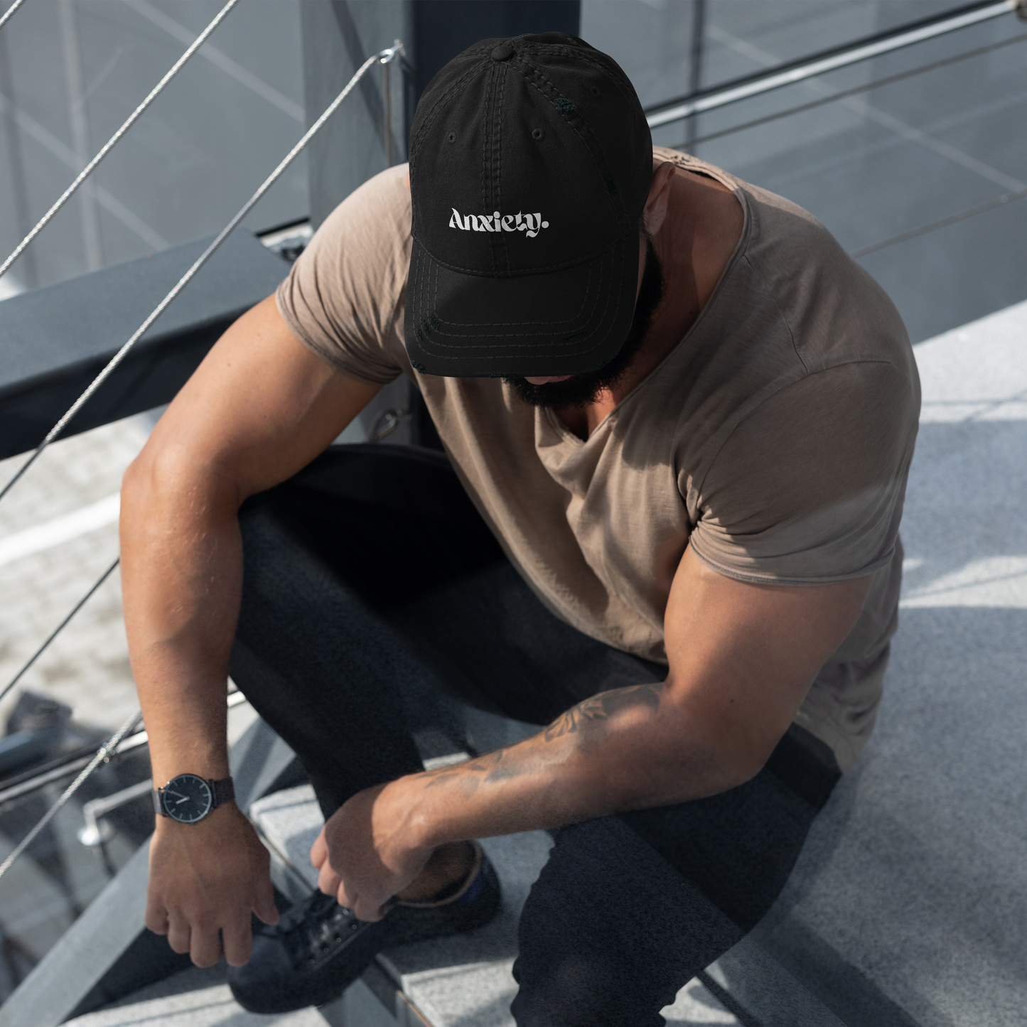 Man sitting on stairs wearing a black cap and brown t-shirt.