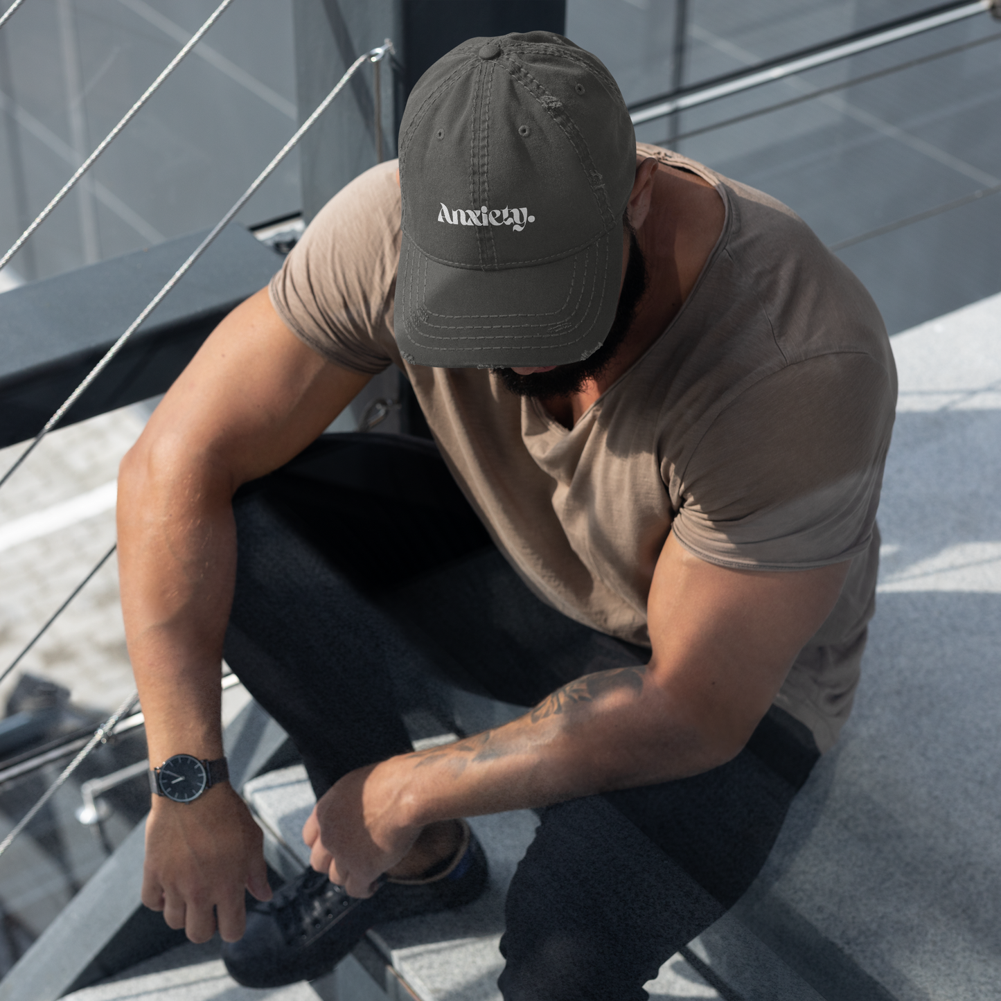 Man wearing a cap and t-shirt, sitting on a metal structure.