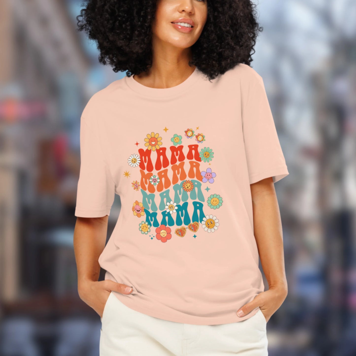 Woman wearing a pink t-shirt with 'MAMA' text and floral designs in an urban setting