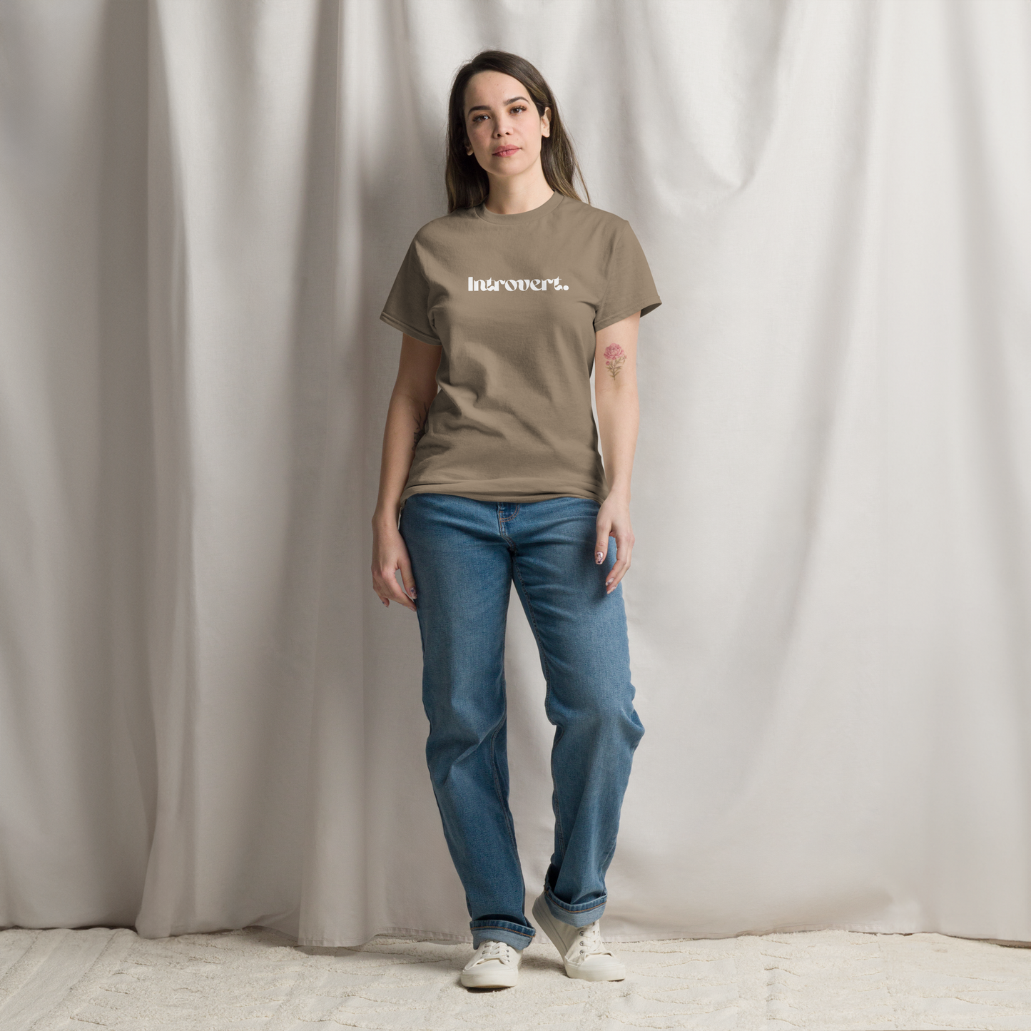 Woman wearing a brown t-shirt with text and blue jeans against a plain background