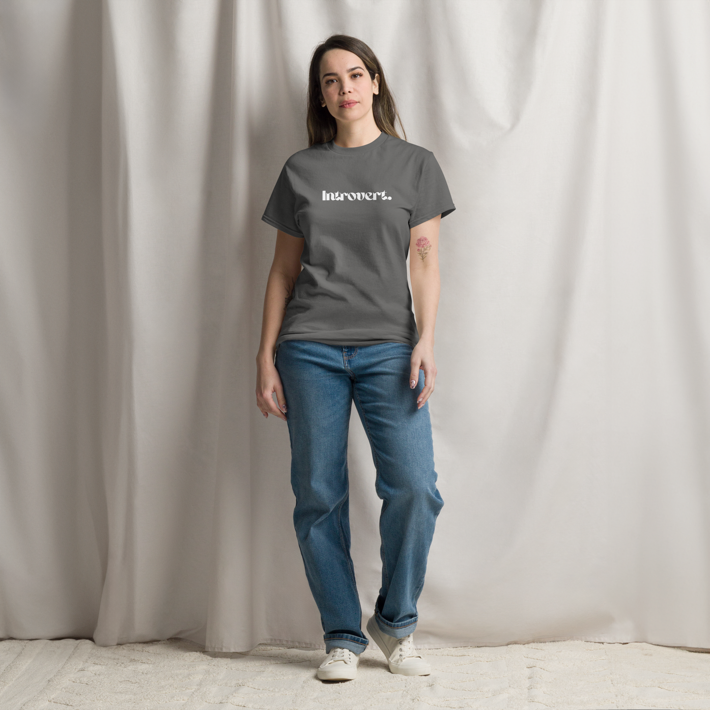 Person wearing a gray t-shirt with text and blue jeans against a plain background