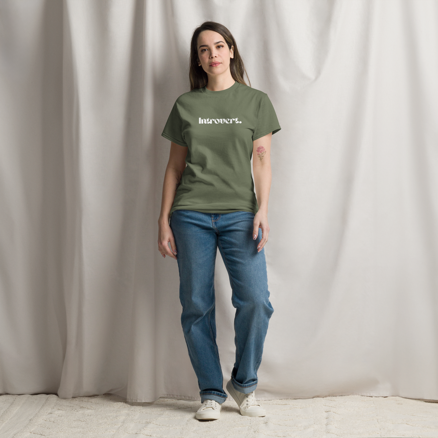 Person wearing a green t-shirt with text and blue jeans against a plain background