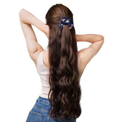 Woman with long wavy hair wearing a floral hair tie on a white background