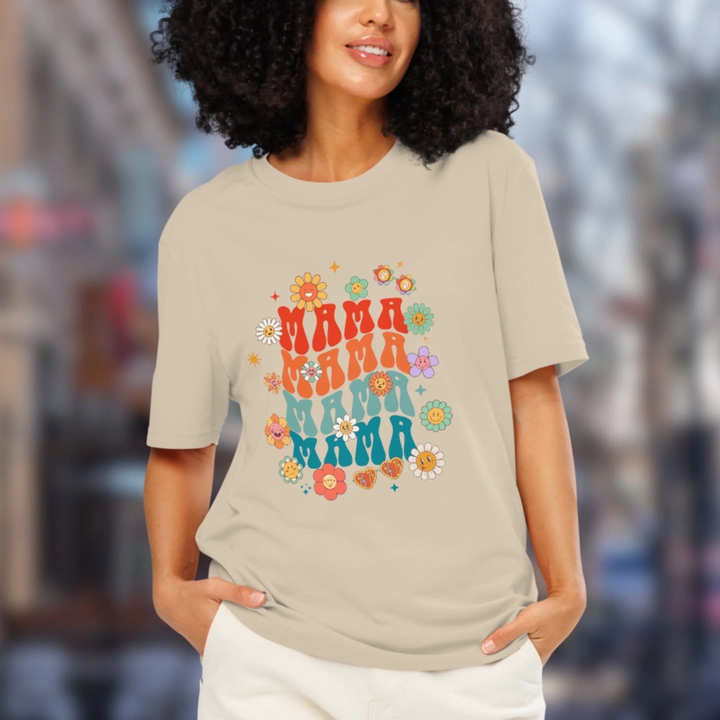 Woman wearing a beige t-shirt with 'MAMA' text and floral designs in an urban setting