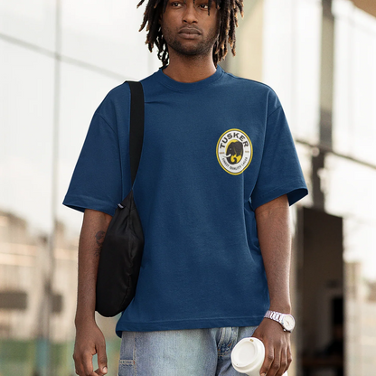 Man wearing a blue t-shirt with a logo, carrying a black bag and holding a white cup.