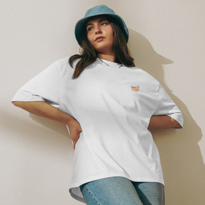 Person wearing a white t-shirt and blue jeans with a green bucket hat against a beige wall.