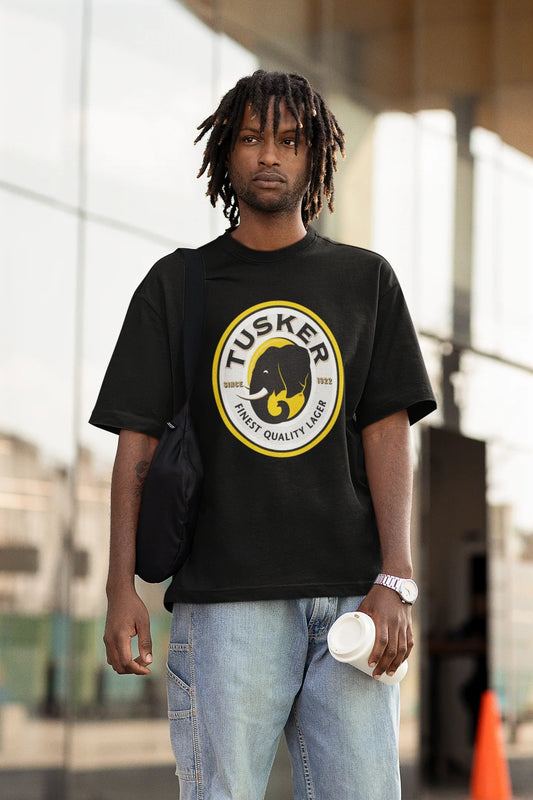 Person wearing a black Tusker t-shirt with a yellow logo, standing outdoors.